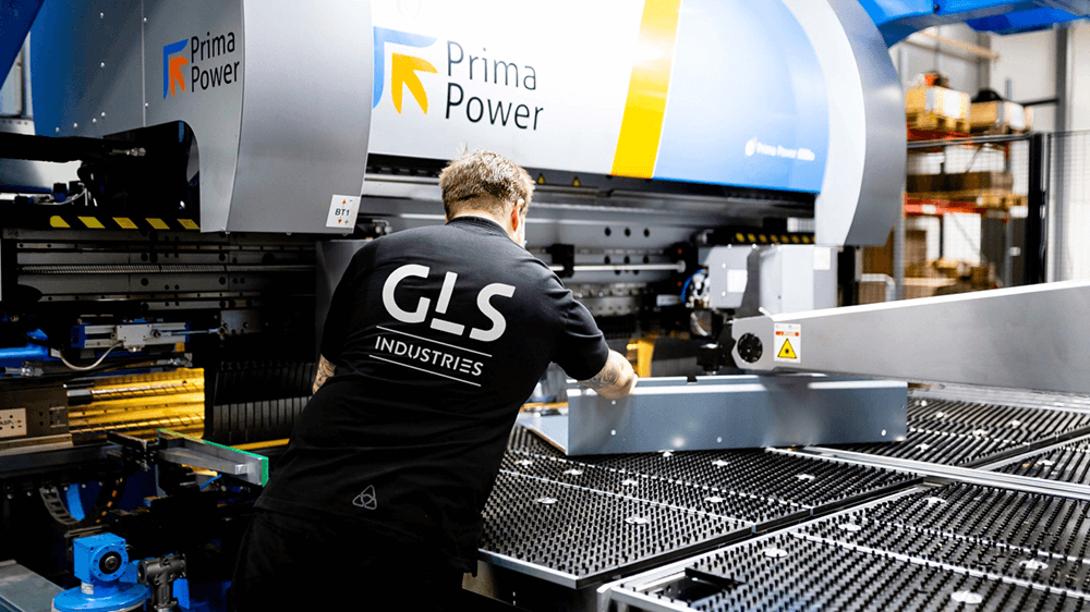 En medarbetare på GLS Industries använder en Prima Power-maskin i en ljus, modern industrimiljö och hanterar med precision en stor metallplåt på arbetsytan.