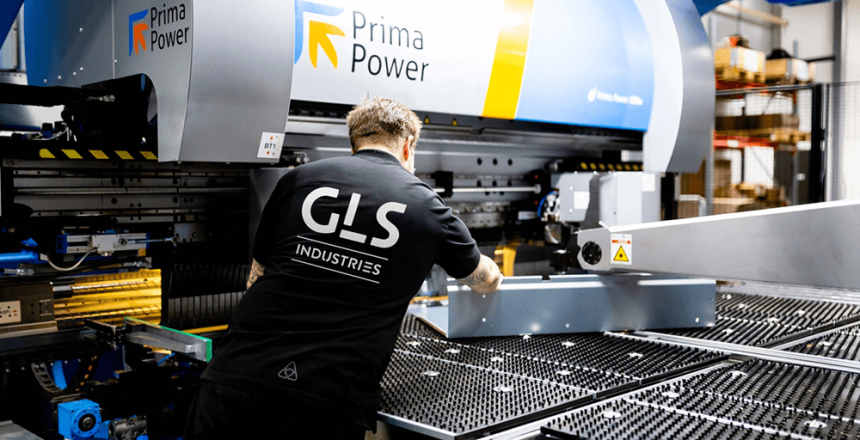 En medarbetare på GLS Industries använder en Prima Power-maskin i en ljus, modern industrimiljö och hanterar med precision en stor metallplåt på arbetsytan.